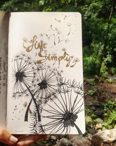 someone is holding up a book with the words live simply written on it and dandelions blowing in the wind