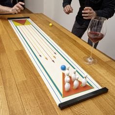 two men playing a game of bowling on a wooden table with wine glass and pins