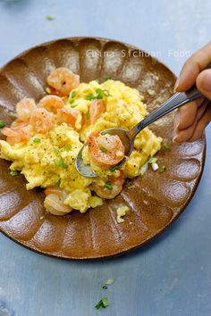 a person holding a spoon over a plate with scrambled eggs and shrimp