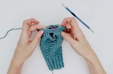 two hands are working on a knitted object with yarn in the shape of a fish