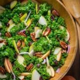 a bowl filled with broccoli, apples and pecans on top of a wooden table