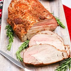 sliced pork roast on a cutting board with rosemary sprigs next to the meat