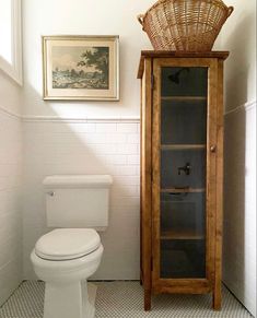 a white toilet sitting next to a tall wooden cabinet in a bathroom under a window