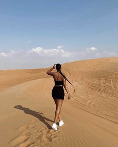 a woman walking across a sandy field