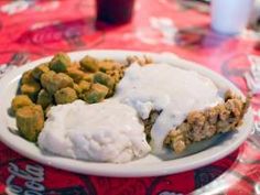 a white plate topped with meat and veggies covered in gravy next to mashed potatoes