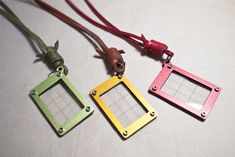 three different colored metal tags on a white surface with a red leather cord attached to them