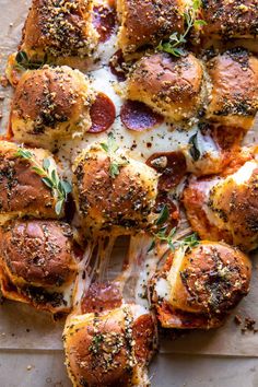 hot dogs covered in cheese and pepperoni on a sheet of baking paper with sprinkled herbs