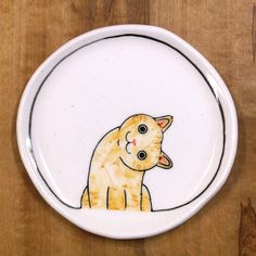 a plate with a drawing of a cat sitting on it's side and looking at the viewer