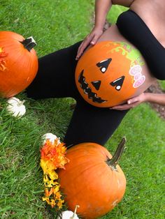 a pregnant woman with painted pumpkins on her stomach in the grass next to flowers