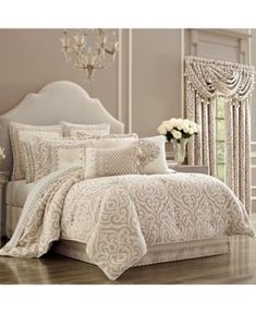 a white bed in a bedroom next to a chandelier and table with flowers