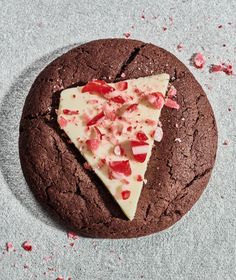 a chocolate cookie with white cheese and strawberries on top, sitting on a gray surface