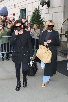 two women walking down the street while holding onto their purses and talking on cell phones