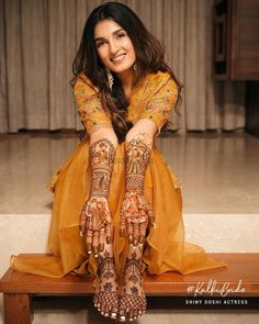 a woman sitting on top of a wooden bench wearing henna and holding her hands up