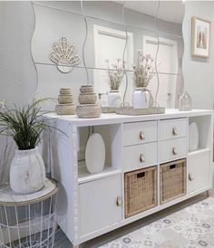 a white dresser with baskets and vases sitting on it's top shelf next to a mirror