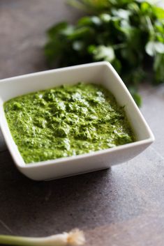 a small white bowl filled with green sauce next to some greens on a table top