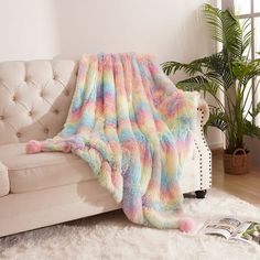 a white couch sitting next to a window covered in a rainbow colored blanket and pillows