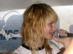 a woman holding a microphone up to her mouth and singing into the microphone while standing in front of a wall