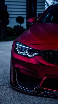 the front end of a red car parked on a driveway in front of a house