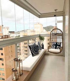 a balcony with a swing chair and pillows on the windowsill overlooking cityscape