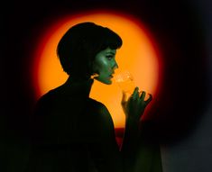 a woman holding a wine glass in front of an orange circle with the sun behind her