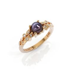 a gold ring with a black pearl and diamonds on the side, in front of a white background