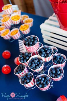 blueberries are arranged in small cups on a table with red and white striped buckets