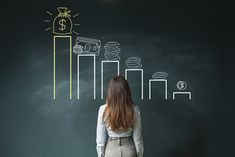 a woman standing in front of a chalkboard drawing on it with money and coins