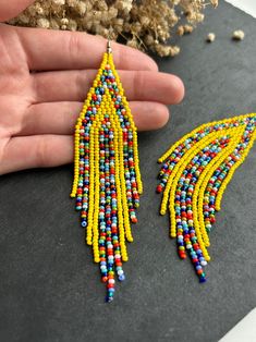 a pair of yellow and blue beaded earrings on a black surface next to dried flowers