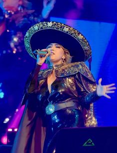 a woman in a costume and hat on stage with her hands out to the side