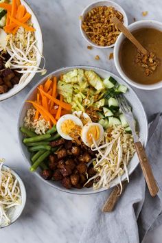 two bowls filled with different types of food on top of a white countertop next to spoons