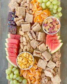 a platter filled with fruit and crackers on top of a wooden table next to grapes