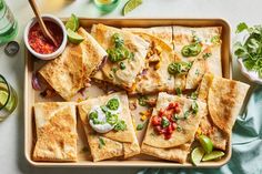 several quesadillas on a tray with salsa and limes