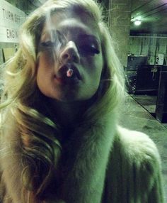 a woman with long blonde hair blowing out her tongue while wearing a fur coat and posing for the camera