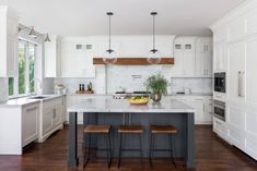 a large kitchen with white cabinets and wood flooring on the walls, along with two stools at the center island