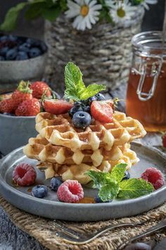 a stack of waffles topped with berries and mint leaves on a gray plate