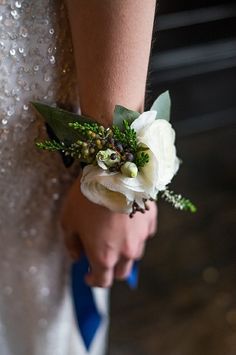 a woman in a wedding dress holding a bouquet of flowers and greenery on her arm