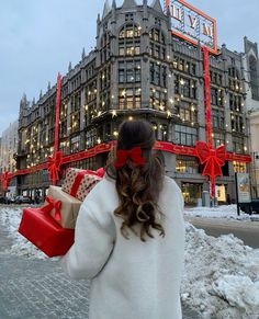 a woman is walking down the street with presents in front of a building that has christmas lights on it