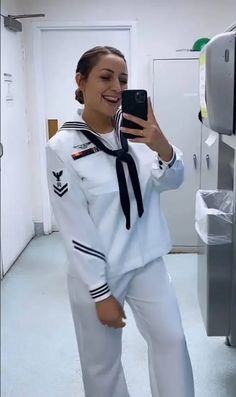 a woman in a navy uniform taking a selfie with her cell phone and smiling