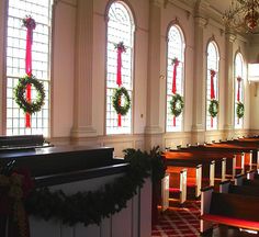 rows of pews with wreaths on them in front of three stained glass windows