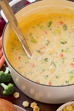 a bowl of broccoli cheese soup next to some carrots and other vegetables