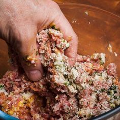 someone is mixing food in a bowl with their hand on top of the meat mixture