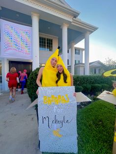 two people dressed as bananas holding a sign