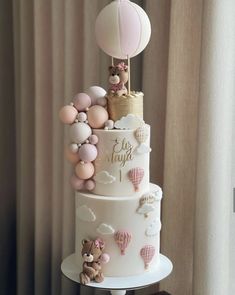 a three tiered cake with balloons and teddy bears on the top is decorated in pastel colors