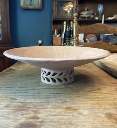 a white bowl sitting on top of a wooden table next to a shelf with pictures