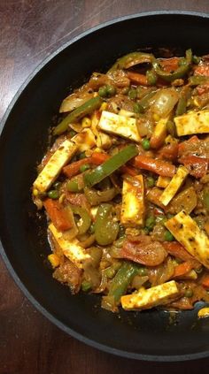 a pan filled with tofu and vegetables on top of a wooden table