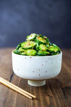 a white bowl filled with green vegetables next to chopsticks