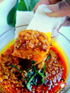 a person holding up a piece of food in a glass bowl with sauce on it