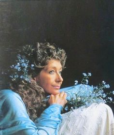 a woman with curly hair and blue sweater holding a bouquet of flowers in front of her face