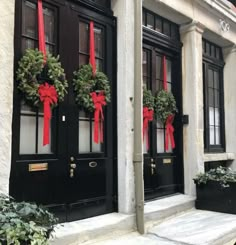 two black doors with red bows and wreaths on the side of them are decorated for christmas