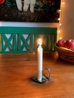 a lit candle sitting on top of a wooden table next to apples and a basket